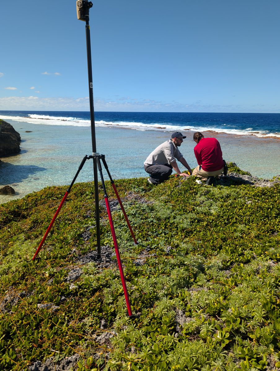 Two field team members document a coral sample beside a GPS base station at Anaraura, Mauke.