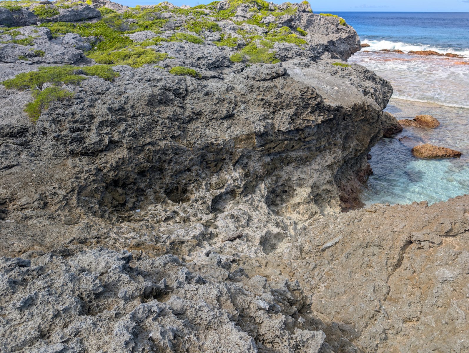 South-coast reddish outcrop: The lower south-coast Mitiaro outcrop is reddish and fades upward without a sharp top; weathering or preservation cause remains uncertain.