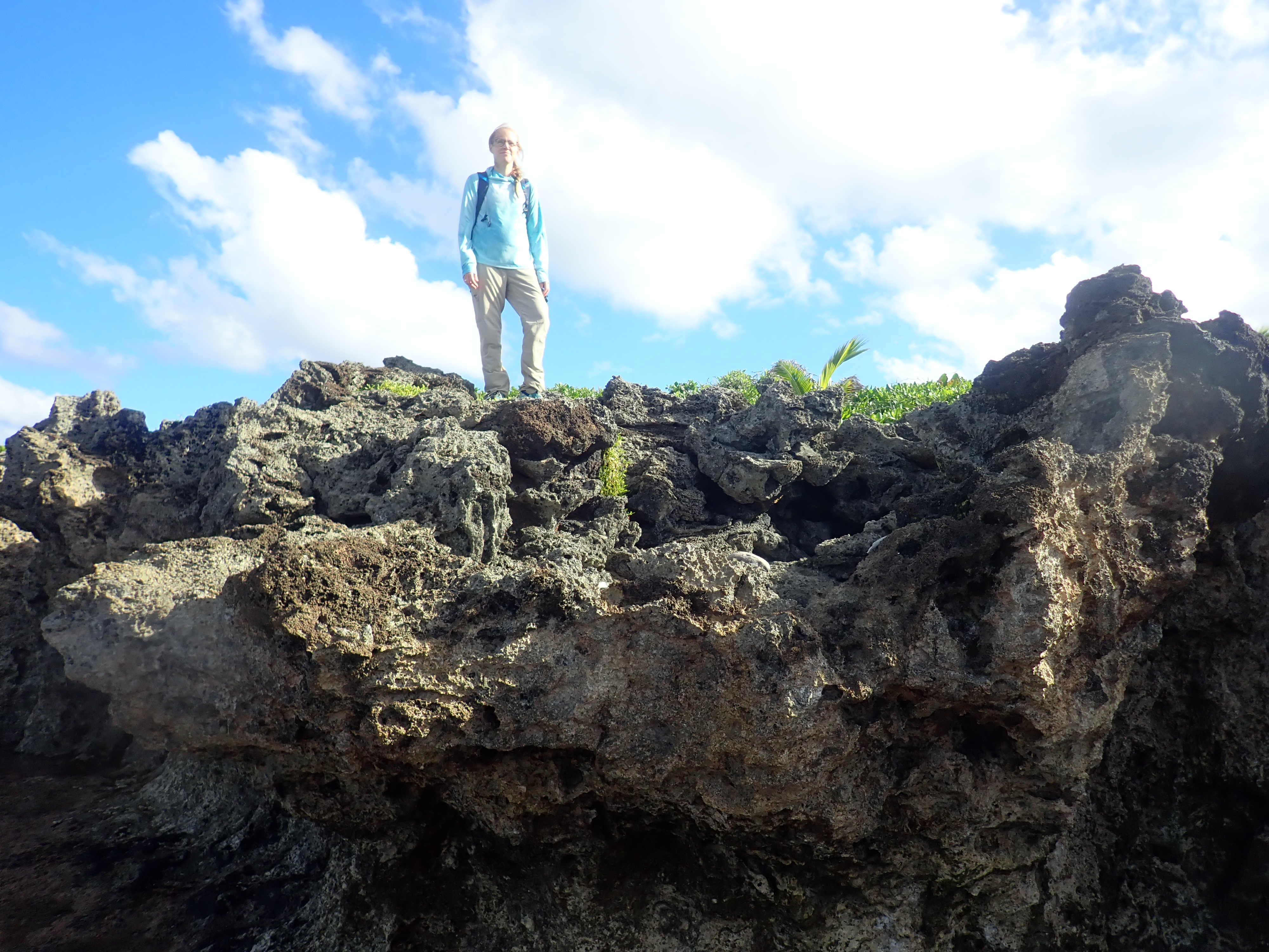 Jacky standing above a deeply weathered dark coastal rock ledge under a blue and cloud-filled sky.