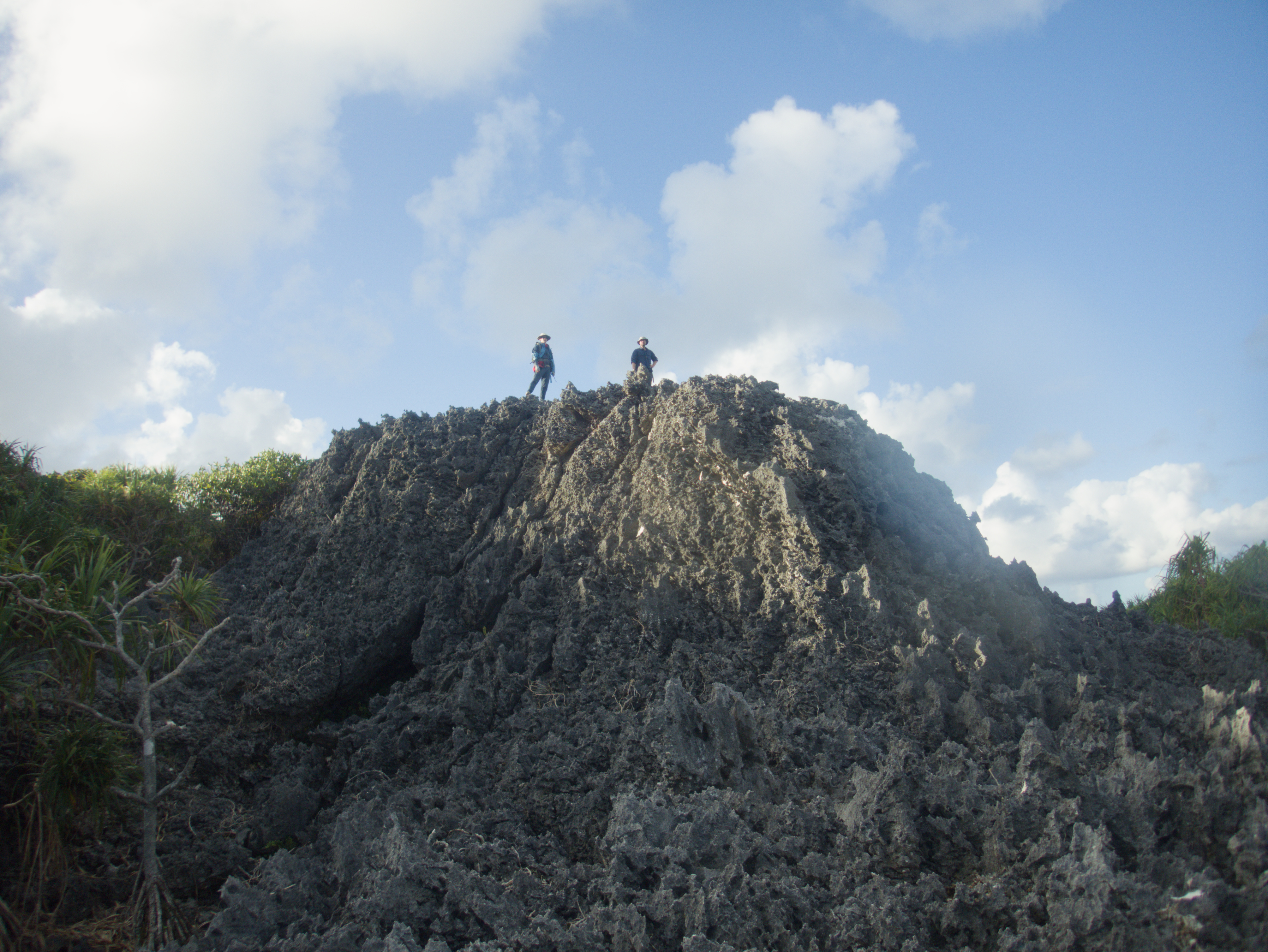 Two researchers stand above deep cracks on the sharp inland makatea at HS109.